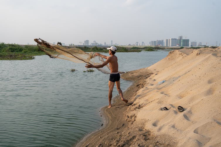 construction worker launching net into river from sandy bank